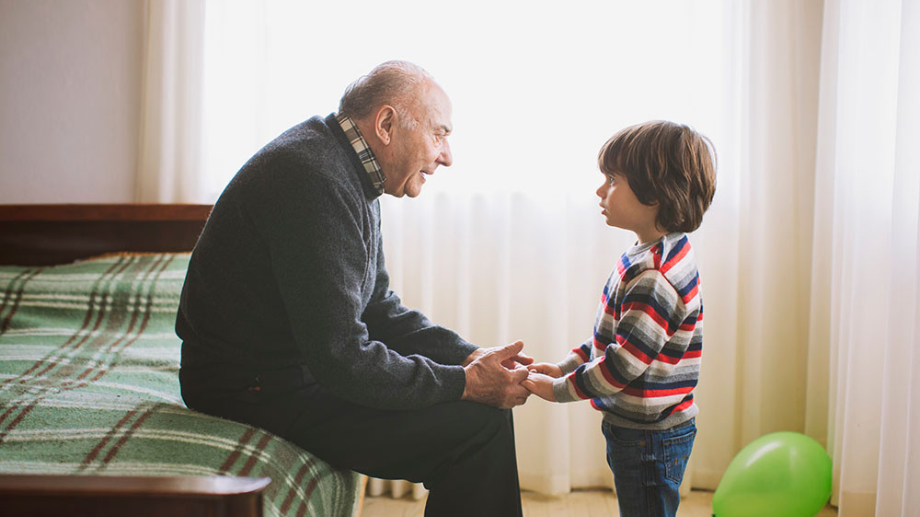 äldre man sitter på sängkant och pratar med pojke